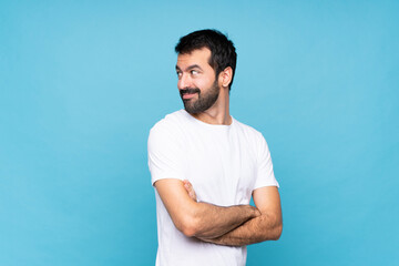 Young man with beard  over isolated blue background with arms crossed and happy
