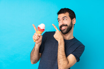 Young man with a cornet ice cream over isolated blue background pointing with the index finger a...