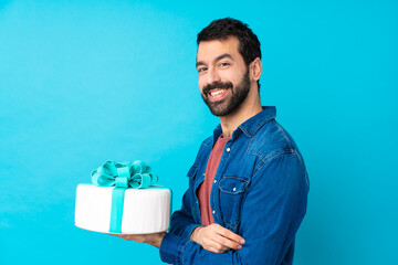 Young handsome man with a big cake over isolated blue background with arms crossed and looking forward