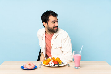 Man at a table having breakfast waffles and a milkshake with arms crossed and happy