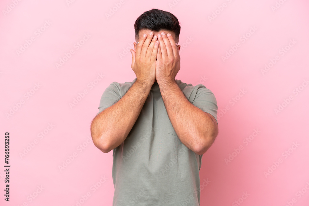 Poster Young caucasian handsome man isolated on pink background covering eyes by hands