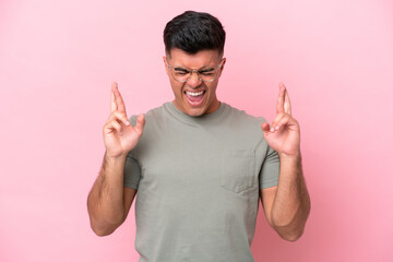 Young caucasian handsome man isolated on pink background with fingers crossing