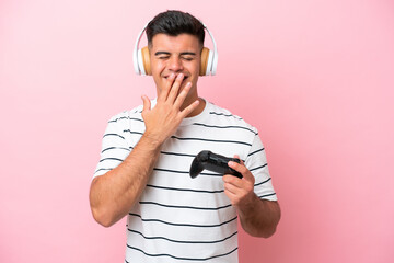 Young handsome man playing with a video game controller isolated on pink background happy and smiling covering mouth with hand