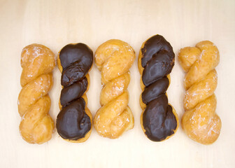 Flat Lay Top View of glazed and chocolate covered twist donuts on a light wood surface, alternating pattern