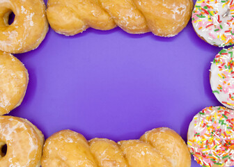 Flat Lay Top View of a variety of donuts forming a border around a vibrant purple background.