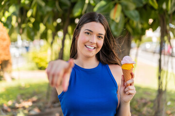Young pretty Brazilian woman with a cornet ice cream at outdoors points finger at you with a...