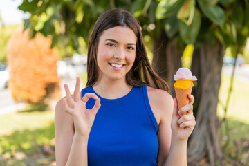 Young pretty Brazilian woman with a cornet ice cream at outdoors showing ok sign with fingers