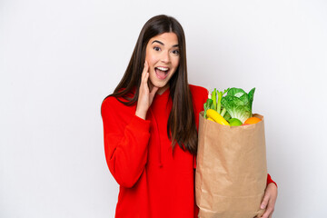 Young Brazilian woman holding a grocery shopping bag isolated on white background with surprise and shocked facial expression