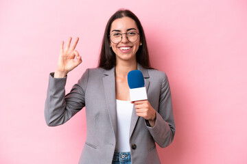 Young caucasian tv presenter woman isolated on pink background smiling and showing victory sign