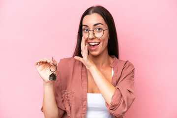 Young woman holding home keys isolated on pink background whispering something