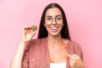 Young caucasian woman holding a Bitcoin isolated on pink background with surprise facial expression