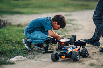 Focus frame on a boy examining a turned over toy car on a dirt road.