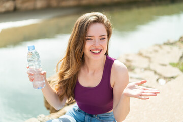 Young redhead woman with a bottle of water at outdoors with shocked facial expression