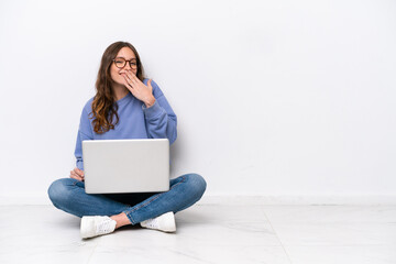 Young caucasian woman with a laptop sitting on the floor isolated on white background happy and...