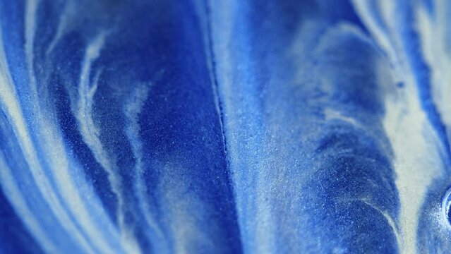 Glitter paint flow. Shimmering texture. Snow cascade. Defocused blue white color sparkling ink emulsion spill motion abstract art background.