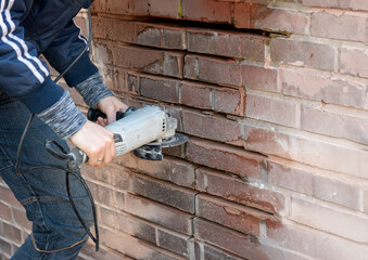 Repairing broken brick wall. Women cleaning grouts with a grinder.