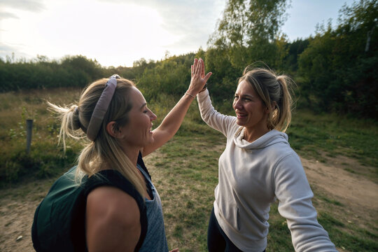 Two female joggers or hikers sharing a high-five, symbolizing teamwork and success on a nature trail during a sunny day.

