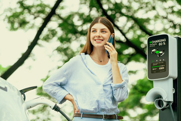 Young woman using smartphone online banking application to pay for electric car battery charging...
