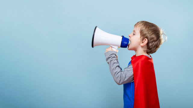 Child in superhero costume using megaphone. Blue background with copy space - Powered by Adobe