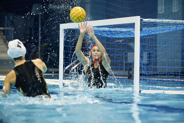 Young active woman in swimwear splashing water and catching ball of rival team while standing on...