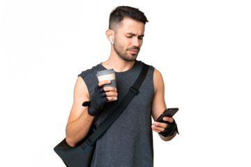 Young sport caucasian man with sport bag over over isolated chroma key background holding coffee to take away and a mobile