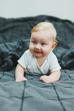 A small four-month-old boy in a white bodysuit is lying in bed and smiling. A smiling baby