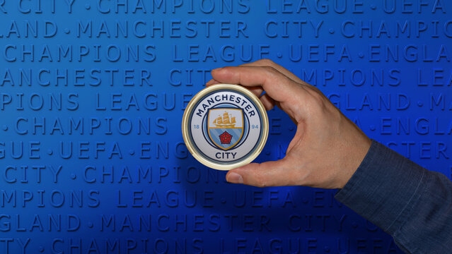 A male hand holds a badge with the emblem of the Manchester City Football Club on blue background. English Soccer Team.