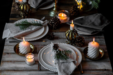Rustic Scandinavian style zero waste eco-friendly dinner table decor for Christmas or new year family celebration. Wooden table, natural elements like pine cones, fir tree branches, candles