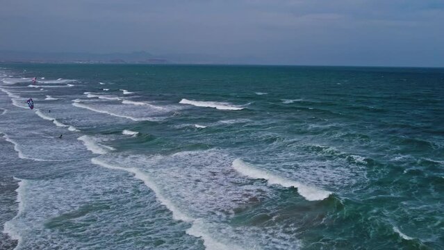 A kitesurfers with a parachute moves through the sea waves. Aerial footage of a fabulous sea tide on a stormy day. Drone footage of crashing surf with foam