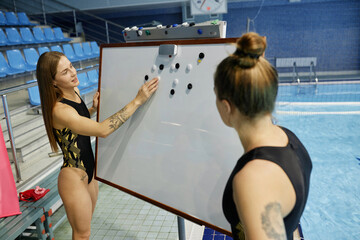 Young confident female water polo trainer operating with small black and white magnets on blank...