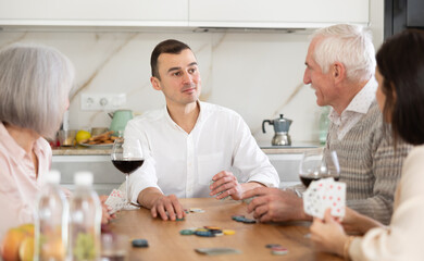 Senior married couple are having fun in cozy home atmosphere, playing card game poker with middle-aged spouses friends. Player makes lead move and believes in luck, emotionally waiting for victory - Powered by Adobe