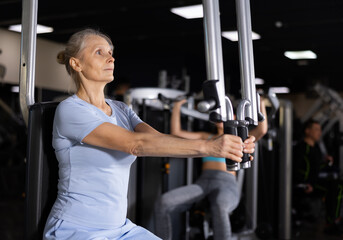 Portrait of elderly woman during workout with power exercise machine in gym club
