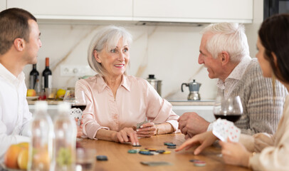 Senior married couple are having fun in cozy home atmosphere, playing card game poker with...