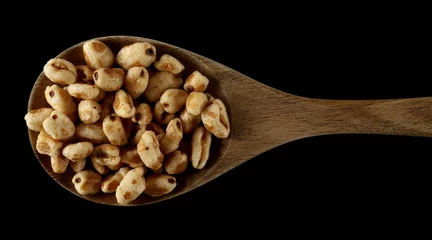 Poster Puffed wheat cereal flakes in wooden spoon isolated on black, top view © dule964