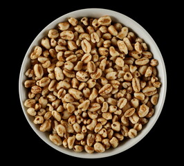 Puffed wheat cereal flakes in bowl isolated on black, top view - 766629492