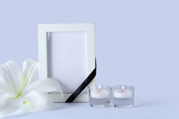 Blank funeral frame, burning candles and beautiful lily flower on grey background