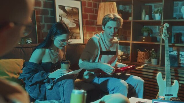 Over shoulder footage of indie rock band members discussing lyrics for new song and laughing while spending evening in old-school studio