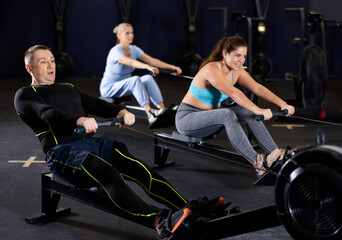 Fototapeta na wymiar Motivated sporty adult man doing strength training, working out on rowing machine in modern gym