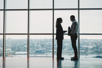 A man and a woman are standing in the office against the background of a large panoramic window....