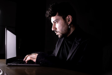 Concentrated man working on laptop in dark room