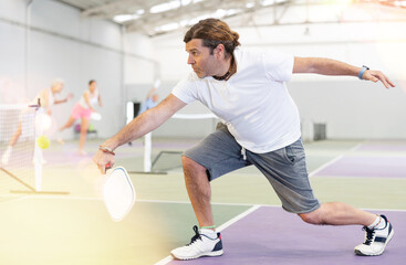 Focused adult man playing friendly pickleball match on small closed court. Concept of concentration in competition..