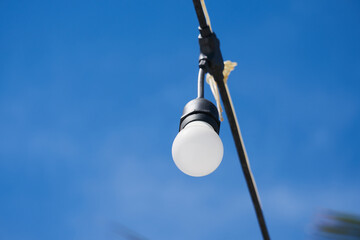 Light bulb on a wire with blue sky on the background.