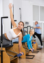 Positive young woman raising arm and stretches lateral muscles of torso while doing pilates...