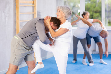 Sportive aged woman practitioner of self-defense courses applying attack methods on her partner