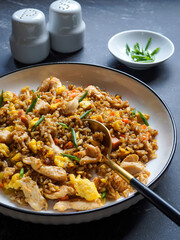 Homemade chicken egg fried rice with vegetables, served on a plate with a spoon. Selective Focus. Dark background.