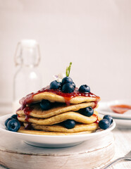 Gluten free blueberry pancakes with berry sauce and fresh blueberry on a white round saucer. Milk bottle as background. Selective focus.