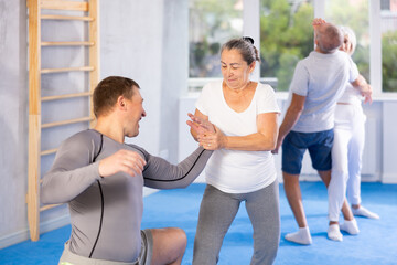 Sportive aged lady practicing arm twist technique against her partner during self-defense courses