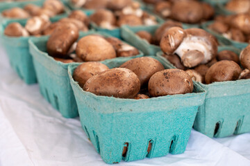 Button mushrooms or cremini or baby bella mushrooms are piled up in green cardboard containers on a white shelf of a grocery store. The brown cultivated organic raw fungi vegetable is freshly picked. © Dolores  Harvey