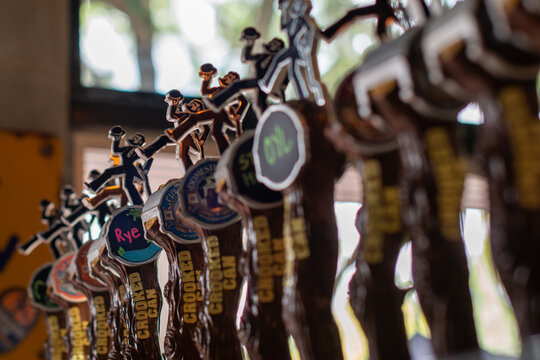 Orlando, Florida, US- April 1, 2024: Crooked Can Brewery's draught beer taps. The handles are high stepper figurines. Men with beards wearing black formal wear and carrying black top hats dancing.