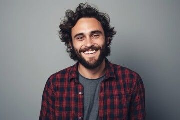 Handsome young man in a plaid shirt smiling at the camera while standing against grey background